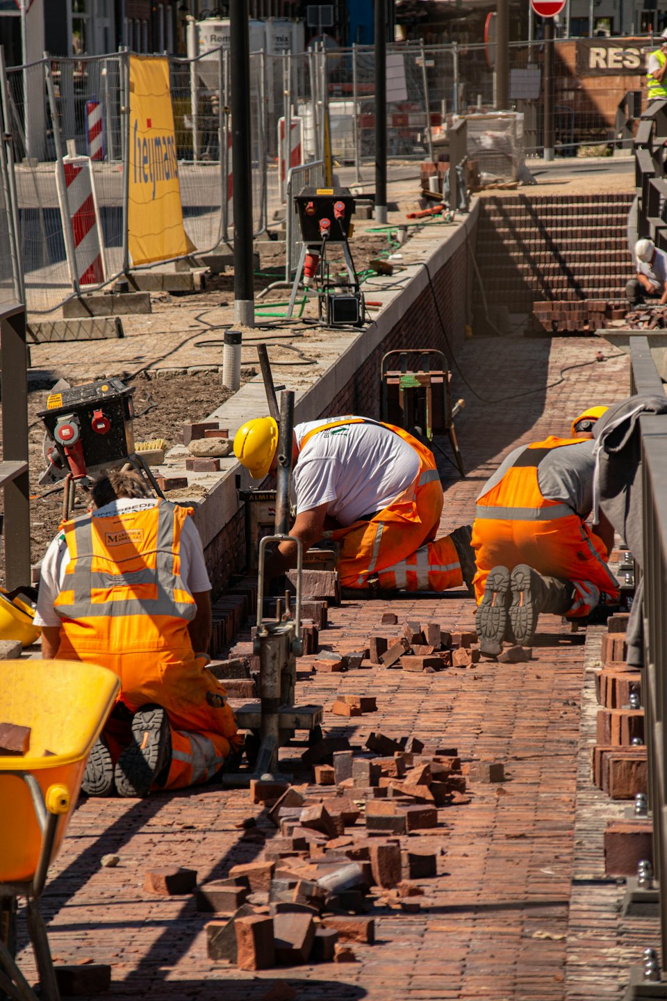 Construction workers in high-visibility gear laying bricks on a pathway.